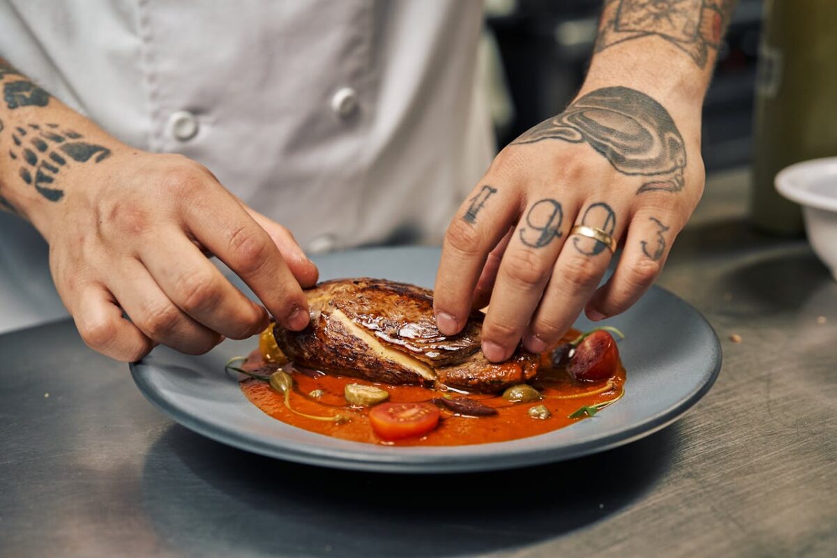 A chef with tattoos skillfully plates a gourmet dish in a professional kitchen.